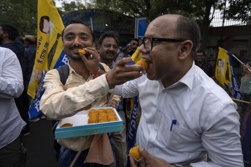 Supporters of the Aam Aadmi Party offer sweets to each other as they wait for the release of the party leader Arvind Kejriwal from Tihar Jail in New Delhi, India, Friday, May 10, 2024. The Supreme Court ordered Arvind Kejriwal's temporary release enabling him to campaign in the country's national election until the voting ends on June 1. (AP Photo /Altaf Qadri)