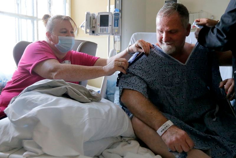 Atlanta Matheson helps tie the hospital gown worn by her husband, Charles Matheson, at Northeast Georgia Medical Center in Gainesville. Visiting restrictions are slowly being eased at the hospital, with each patient being allowed two visitors. (Christine Tannous / Atlanta Journal-Constitution)