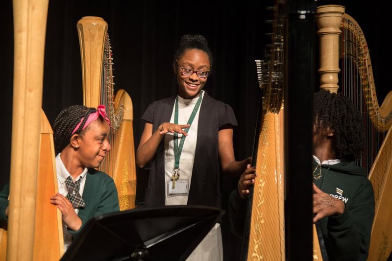 Harp teacher Angelica Hairston (center) talks with Drew Charter School freshman Nailah Williams (left) and Afiya Cave during a recent practice at the Drew Charter School. STEVE SCHAEFER / SPECIAL TO THE AJC