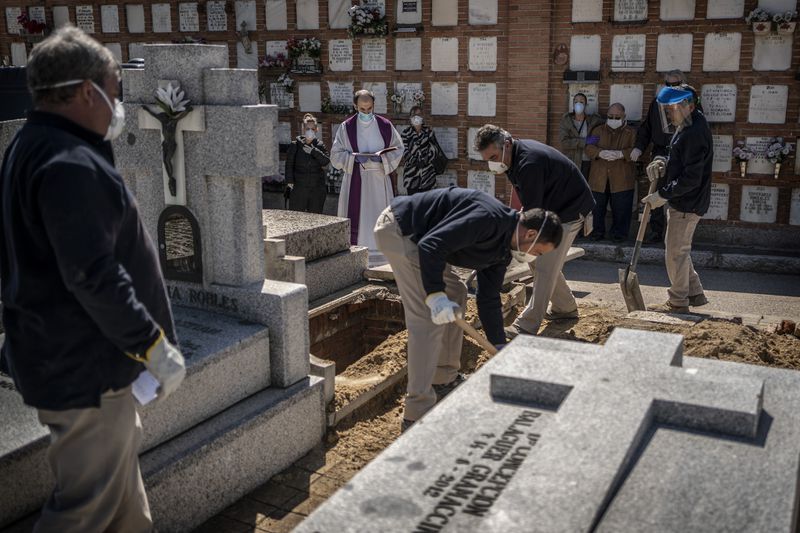 A priest and relatives pray as a victim of the COVID-19 coronavirus is buried by undertakers at the Almudena cemetery in Madrid.