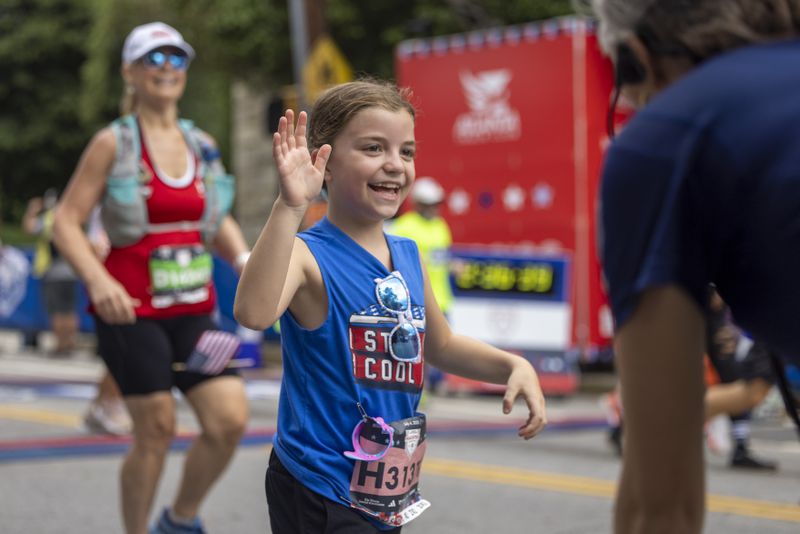 In this file photo from July 4, 2023, a young runner gets a high five after shecro sses the finish line during the running of the Atlanta Journal-Constitution Peachtree Road Race at Piedmont Park. Jason Getz / Jason.Getz@ajc.com)