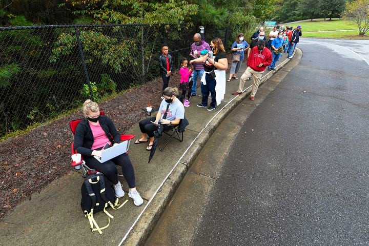 University of Georgia student Courtney Wetzel, from left, participates in a Zoom online class as and her friend Ashley Lee, wait with others in a line to vote that has an estomated 3 hour wait and as the first day of early voting is shown underway on Monday, Oct. 12, 2020, at the George Pierce Park  in Suwanee, Ga. JOHN AMIS FOR THE ATLANTA JOURNAL- CONSTITUTION