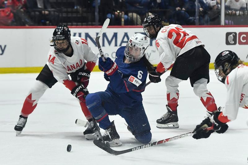 United States' Rory Guilday, center, tries to shoot as she is defended by Canada's Renata Fast, left, and forward Emily Clark during the second period in the final at the women's world hockey championships in Utica, N.Y., Sunday, April 14, 2024. (AP Photo/Adrian Kraus)