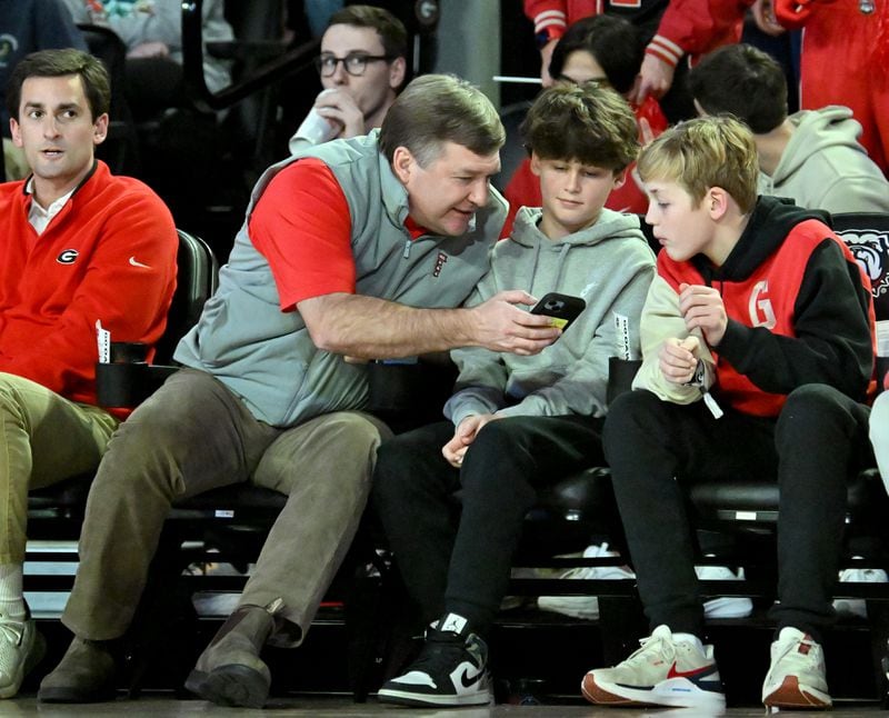 Georgia football head coach Kirby Smart and his son Andrew (right) look at a phone during the first half of an NCAA college basketball game at Stegeman Coliseum, Wednesday, January 24, 2024, in Athens. (Hyosub Shin / Hyosub.Shin@ajc.com)