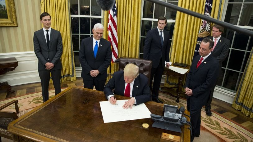 President Donald Trump signs an executive order on his first evening in the Oval Office at the White House in Washington, Jan. 20, 2017. Trump signed a number of executive orders shortly after taking office. At left are Jared Kushner and Vice President Mike Pence. To Trump’s right is Reince Priebus, his chief of staff. (Doug Mills/The New York Times)