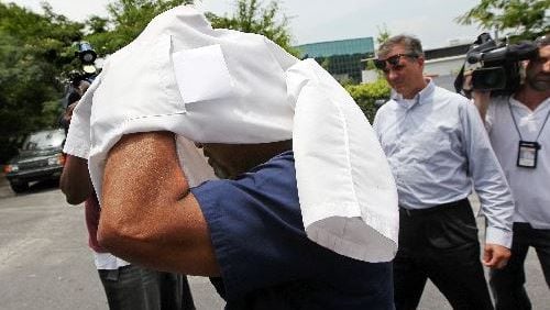 A doctor covers his head as he leaves during a ” pill mill” raid near Tucker in 2012. More than a half dozen patients were taken away in cuffs to a prisoner transport van. The doctors and employees were allowed to leave following the raid. The owner of the business was also removed in cuffs and taken away in a prisoner transport van. CURTIS COMPTON / CCOMPTON@AJC.COM AJC File Photo