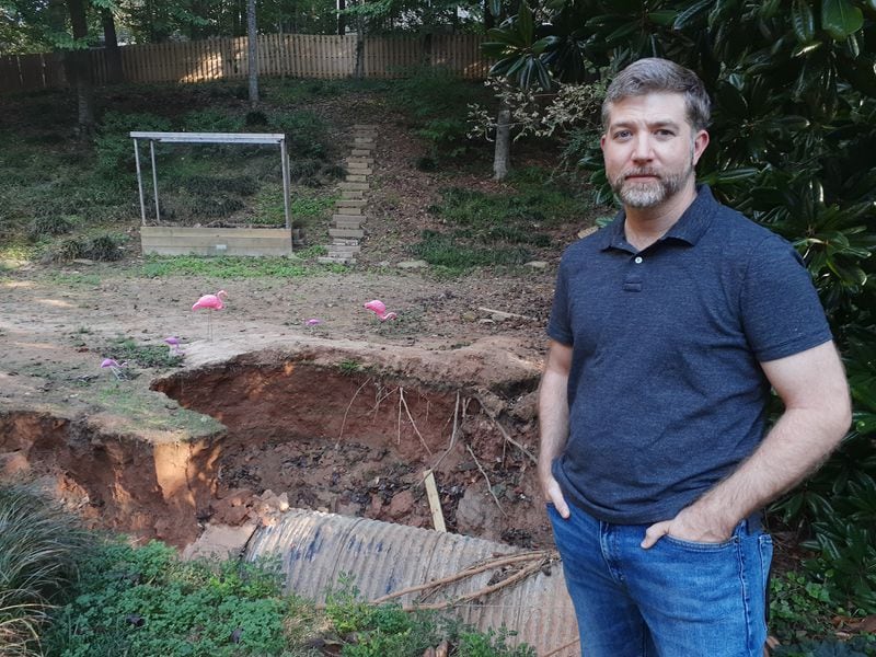 Marietta resident Orion Smith stands in front of a six-foot deep sinkhole that opened up in his backyard after the Sept. 7 flash flood decimated his Weatherstone neighborhood. (Matt Bruce/for the AJC)
