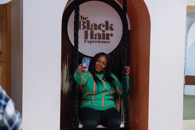 Loreal Smith takes a selfie while sitting on a braid swing at the Black Hair Experience in Atlanta on Saturday, January 28, 2023.  (Natrice Miller/natrice.miller@ajc.com) 