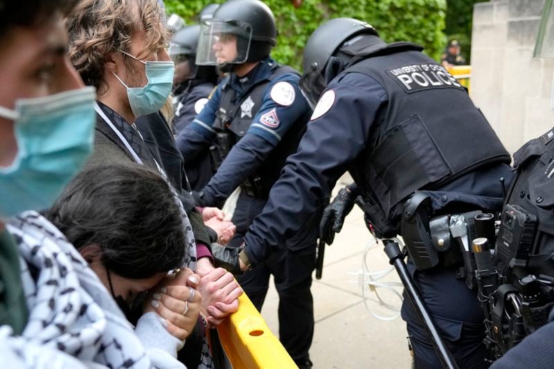 A pro-Palestinian protester rests her head on her clasped hands while she stands before University of Chicago police officers while officers kept protesters from the university's quad while the student encampment is dismantled Tuesday, May 7, 2024, in Chicago. (AP Photo/Charles Rex Arbogast)