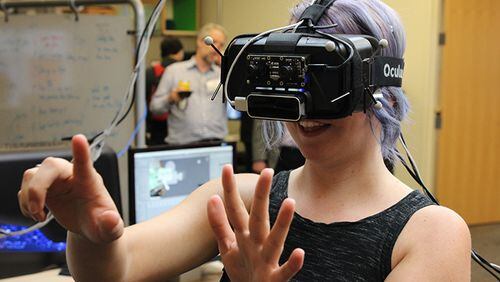 Virtual reality technology plays into expectations about our computing future. One perplexing challenge: people sometimes get nauseous trying to move with the headgear on. Here, the leader of a local VR program development company tries on a  headset at a Georgia Tech event.