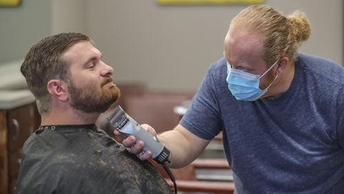 At the Peachtree Battle Barber Shop in Atlanta, barber and owner Chris Edwards wears a mask as he cuts the hair of customer David Boswell on Friday, April 24, 2020. The first phase of Gov. Brian Kemp’s plan to reopen Georgia during the coronavirus pandemic included barber shops, hair salons and gyms, though not all chose to open their doors. JOHN SPINK/JSPINK@AJC.COM