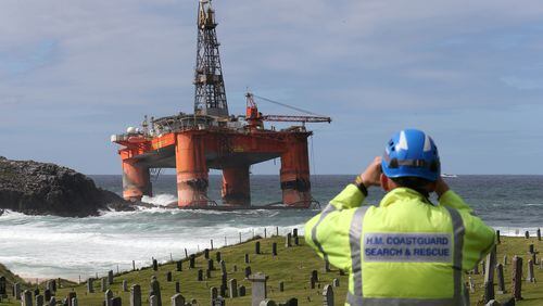 A coastguard official monitors the Transocean Winner drilling rig off the coast of the Isle of Lewis, Scotland, after it ran aground in severe weather conditions, Tuesday Aug. 9, 2016. The oil rig, carrying 280 tonnes of diesel, broke free of its tug and ran aground on the remote Scottish island where it is being monitored by a counter-pollution team. (Andrew Milligan / PA via AP)