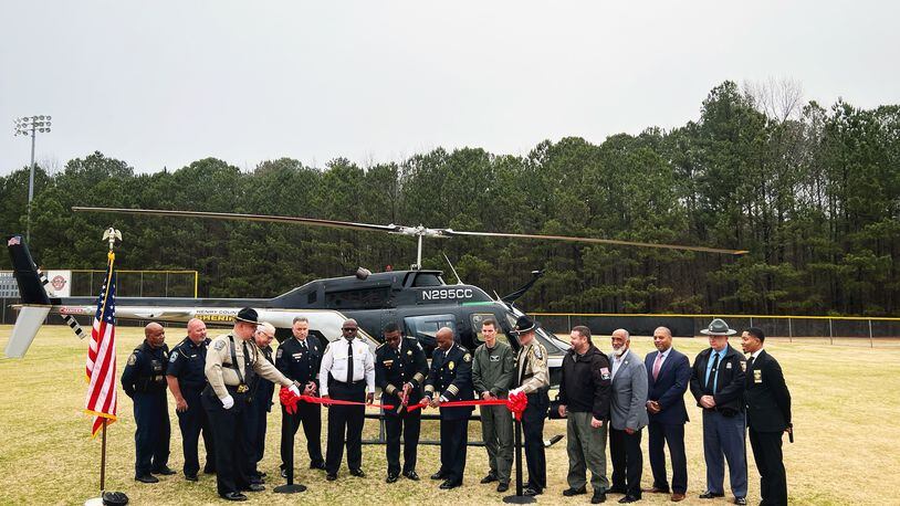 Henry County Sheriff Reginald Scandrett (center) cuts a ribbon in front of his agency's new helicopter while flanked by other leaders from local government and neighboring law enforcement agencies.