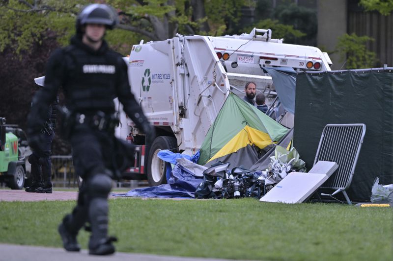 A police officer in riot gear walks past a garbage truck being loaded with the remains of the pro-Palestinian encampment at MIT, which police raided before dawn Friday, May 10, 2024, in Cambridge, Mass. (AP Photo/Josh Reynolds)