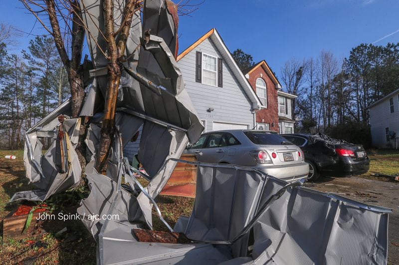 Twisted metal is wrapped around a tree in one yard. In the background, the back window of a car is damaged as well. JOHN SPINK / AJC
