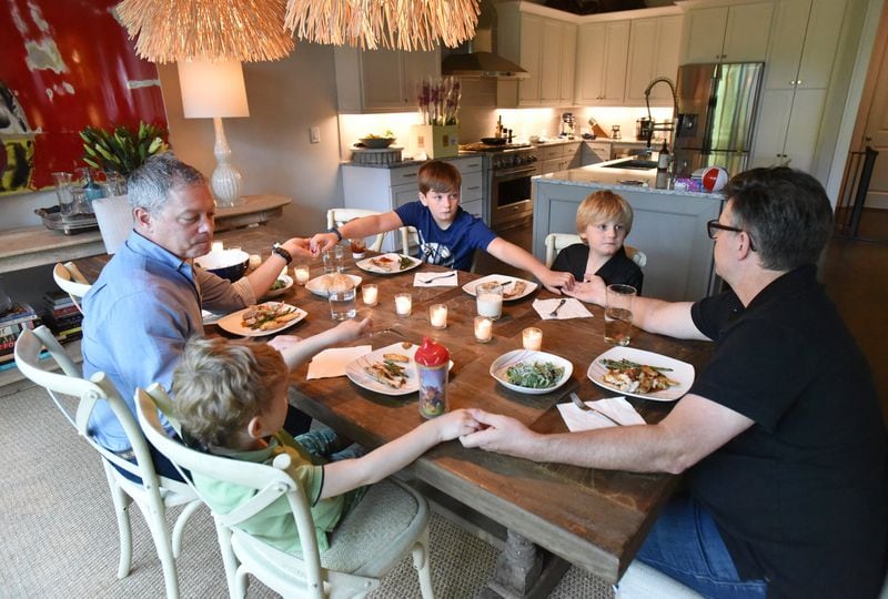 Matthew Simon (left) and Keith Schumann join hands before dinner with sons Owen (lower left), 4, Jackson (center), 10, and Hunter, 6. HYOSUB SHIN / HSHIN@AJC.COM