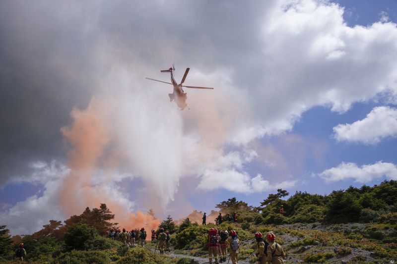A helicopter drops water during a drill, as firefighters in training for the special unit, practice near Villia village some 60 kilometers (37 miles) northwest of Athens, Greece, Friday, April 19, 2024. Greece's fire season officially starts on May 1 but dozens of fires have already been put out over the past month after temperatures began hitting 30 degrees Celsius (86 degrees Fahrenheit) in late March. This year, Greece is doubling the number of firefighters in specialized units to some 1,300, adopting tactics from the United States to try and outflank fires with airborne units scrambled to build breaks in the predicted path of the flames. (AP Photo/Thanassis Stavrakis)
