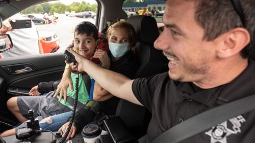 Jose Lopez, 10, sits on his mom Ady Escobar’s lap as Dawson County Sheriff's Deputy Matthew Blackstrap holds the microphone so he can pretend he’s pulling someone over, during Ferrari of Atlanta’s "Rides to Remember" event Saturday morning. The event gives sick children a chance to ride around Atlanta Motorsports Park in Dawsonville in sports cars. (Ben Gray for the Atlanta Journal-Constitution)