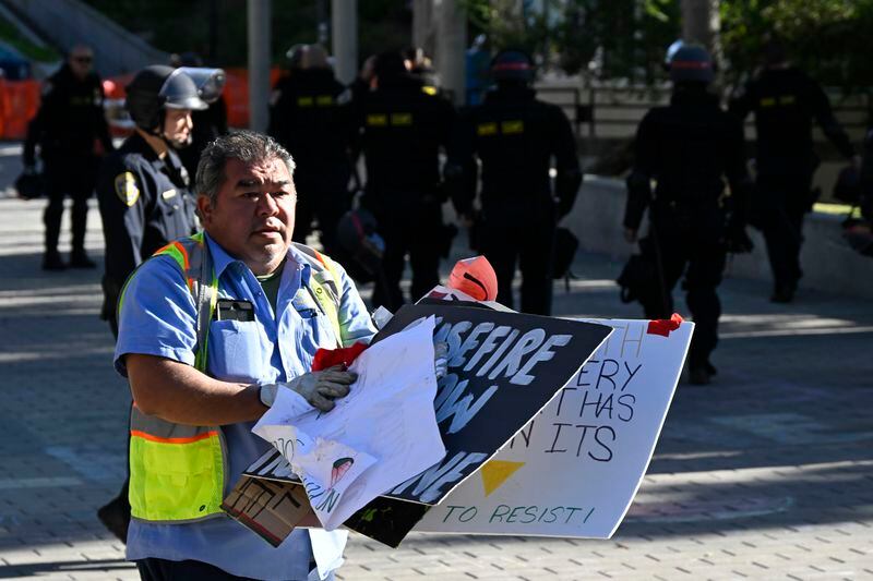 Police officers look on as a worker removes signs from a Pro-Palestinian encampment set up in front of Geisel Library at UC San Diego, Monday, May 6, 2024, in San Diego. Police cleared the campus encampment in the early morning Monday. (AP Photo/Denis Poroy)