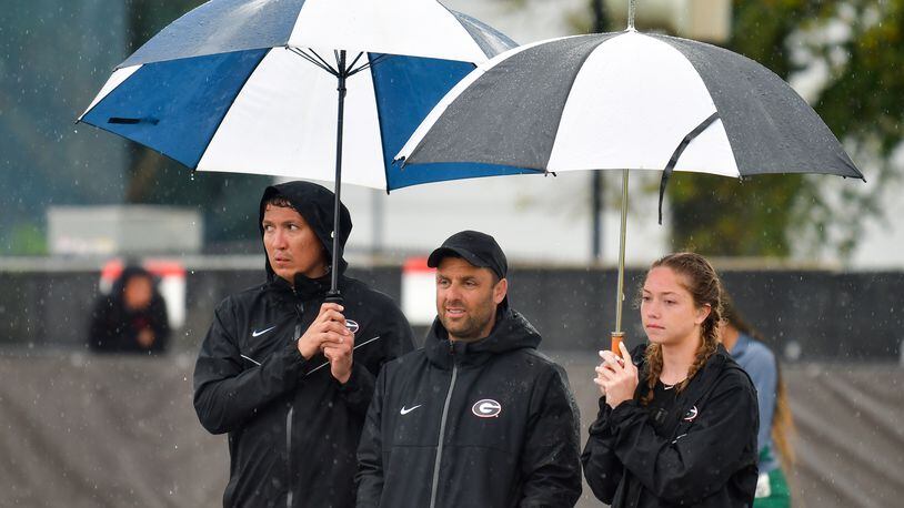 Georgia coach Petro Kyprianou (center) finds some relief from the rain under the umbrellas of a couple of track team members during the Spec Towns Invitational at the Spec Towns Track in Athens on Saturday, April 10, 2021. (Photo by Rob Davis/UGA Athletics)