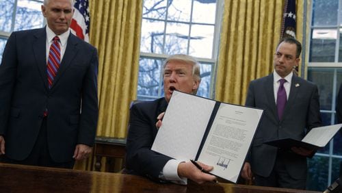 Vice President Mike Pence (left) and White House Chief of Staff Reince Priebus watch as President Donald Trump shows off an executive order to withdraw the U.S. from the 12-nation Trans-Pacific Partnership trade pact on Jan. 23.