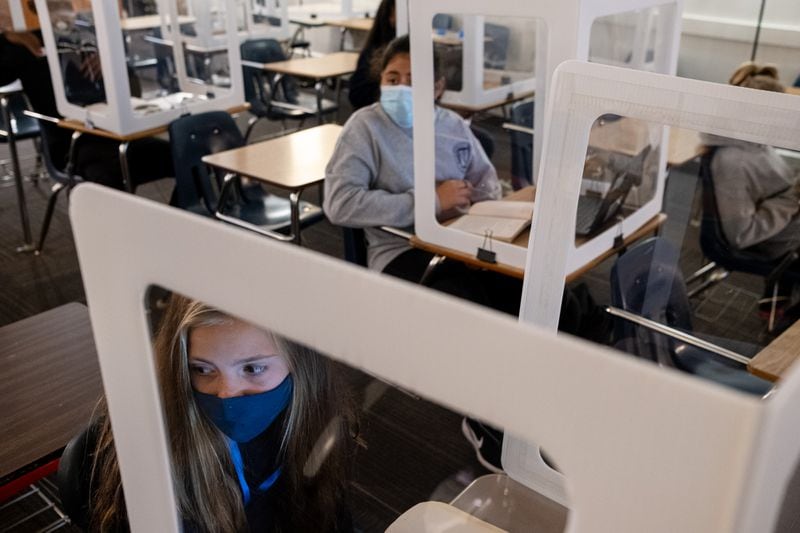 Celeste Martin, left, and Monserrath Guerrero look to their teacher from behind plastic partitions during their language arts class at Marietta Middle School on Thursday afternoon, Nov. 5, 2020. Even though there are only five students in the room during class, they all wear masks and sit behind plastic partitions. (Ben Gray for the Atlanta Journal-Constitution)
