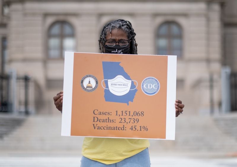 Dr. Marjorie Roberts, a long-haul Covid survivor, poses for a photo outside of the State Capitol on Thursday morning. Roberts brought the sign and one empty folding chair to bring attention to the victims of COVID-19. Ben Gray for The Atlanta Journal-Constitution