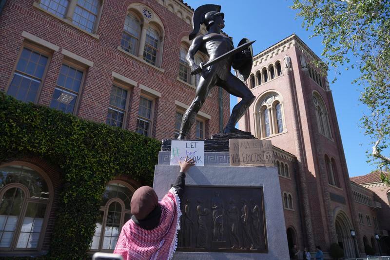 A Pro-Palestinian student places a sign on the Tommy Trojan statue on the campus of the University of Southern California during a protest against the 2024 valedictorian Asna Tabassum canceled commencement speech on Thursday, April 18, 2024. The University of Southern California canceled the commencement speech by its 2024 valedictorian who has publicly supported Palestinians, citing security concerns, a rare decision that was praised by several pro-Israel groups and lambasted by free speech advocates and the country's largest Muslim civil rights organization. (AP Photo/Damian Dovarganes)