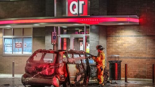 A DeKalb County firefighter douses hot spots after a minivan burst into flames Tuesday morning outside a Brookhaven QuikTrip.