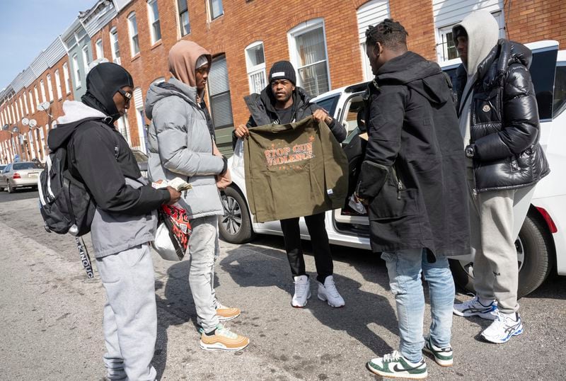Antonio Moore, center, 24, of Baltimore, hands out designer t-shirts reading "Stop Gun Violence" in his childhood neighborhood in east Baltimore, Monday, Feb. 26, 2024. Moore, is a successful real estate investor and entrepreneur who founded a consulting company that helps brands and nonprofits connect with urban youth. (AP Photo/Steve Ruark)
