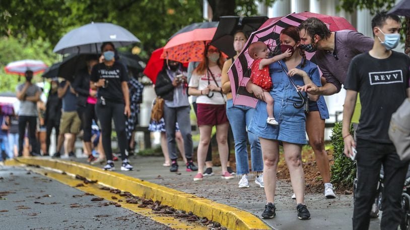 Amanda McElveen holds 1-year old Luna, left, as Justin McElveen interacts while they and other voters stand in line in the rain at Garden Hills Elementary School in Atlanta on Friday, the last day of early voting for the Georgia primary. Lines lasted for hours in some places. JOHN SPINK/JSPINK@AJC.COM