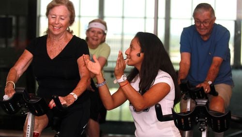 Angela Alvarado, a health coach instructor, helps Patricia Henning, left, during a cycling class for individuals with Parkinson's on Aug. 13, 2015.