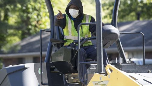 Wearing a medical mask, H.E.H. Paving roller operator Charles Barker works with crews as they lay asphalt on Gwendon Terrace in Decatur. The paving project is part of the DeKalb County Special Purpose Local Option Sales Tax. (ALYSSA POINTER / ALYSSA.POINTER@AJC.COM)