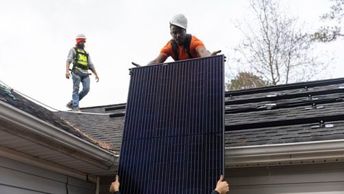 Joe McClain, left, and Mike Harris, right, installers for Creative Solar USA, move solar panels onto the roof of a home in Ball Ground, Georgia on December 17th, 2021.   (Nathan Posner for The Atlanta Journal-Constitution)