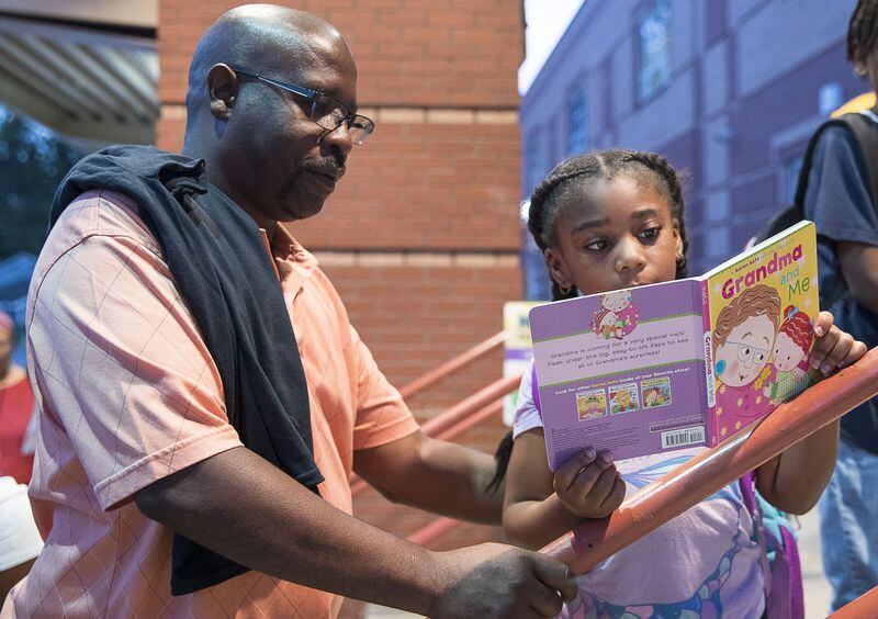 Nathaniel Walker (left) listens as his granddaughter Kasey Walker (right) reads a book she received from Fathers Incorporated at M. Agnes Jones Elementary School in Atlanta’s Ashview Heights neighborhood. ALYSSA POINTER / ALYSSA.POINTER@AJC.COM