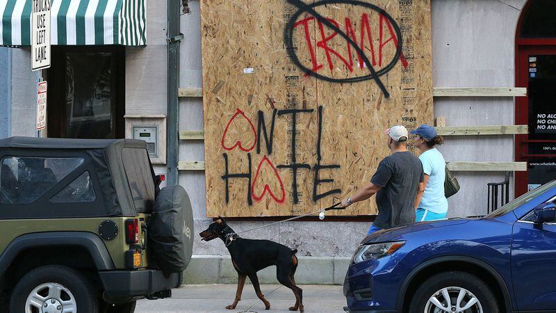 Eric and Nicole Zajkowski, who just evacuated from their home in Coral Springs, Fla., walk their dog Neeko past a   boarded-up store on Savannah's Bay Street Friday. Curtis Compton/ccompton@ajc.com