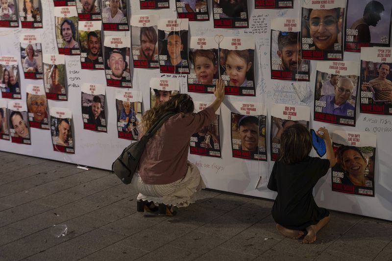 FILE - A woman touches photos of Israelis missing and held captive in Gaza that are displayed on a wall in Tel Aviv, Israel, Oct. 21, 2023. Israel and Hamas appear to be seriously negotiating an end to the war in Gaza and the return of Israeli hostages. A leaked truce proposal hints at concessions by both sides following months of stalemated talks. (AP Photo/Petros Giannakouris, File)