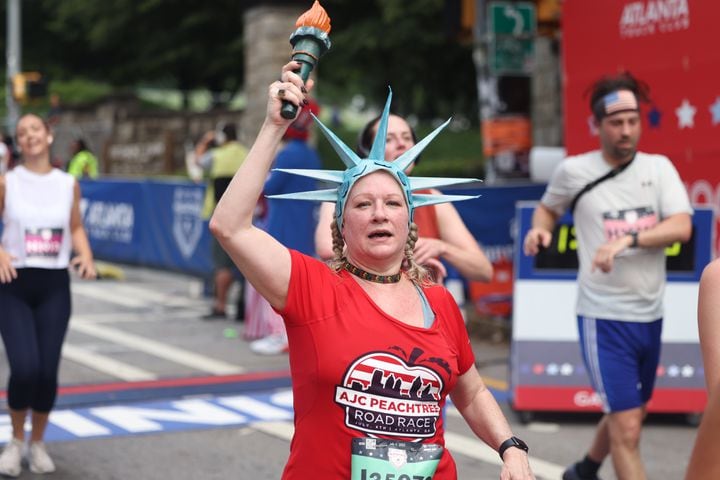 Runner wearing Statue of Liberty crown raises torch at the finish of the 54th running of the Atlanta Journal-Constitution Peachtree Road Race in Atlanta on Tuesday, July 4, 2023.   (Jason Getz / Jason.Getz@ajc.com)