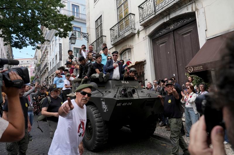 Former army captain Manuel Correia Silva, holding red carnations, arrives at Carmo square in Lisbon, Thursday, April 25, 2024, on the same vehicle he led there fifty year ago, during the reenactment of troops movements, part of anniversary celebrations of the Carnation Revolution. The army led coup restored democracy in Portugal after 48 years of a fascist dictatorship. (AP Photo/Ana Brigida)