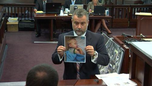 Defense attorney Maddox Kilgore, holding an image of a sleeping Cooper Harris, begins his cross examination of Cobb County lead detective Phil Stoddard on Tuesday. (Screen capture via WSB-TV)