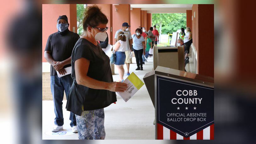 Nina Wilson drops off her absentee ballot while dozens of other voters line up to cast their votes in person on the first day of early voting at the Cobb County Board of Elections & Registration on Monday, May 18, 2020, in Marietta.   Curtis Compton ccompton@ajc.com