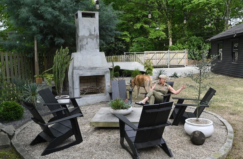 Alison Michaels-Fandel, with her dog Francis, sits by her outdoor fireplace Thursday, April 13, 2023, in Atlanta. Behind her is the concrete skate bowl she had installed for her husband at their Grant Park home. (Hyosub Shin / Hyosub.Shin@ajc.com) 