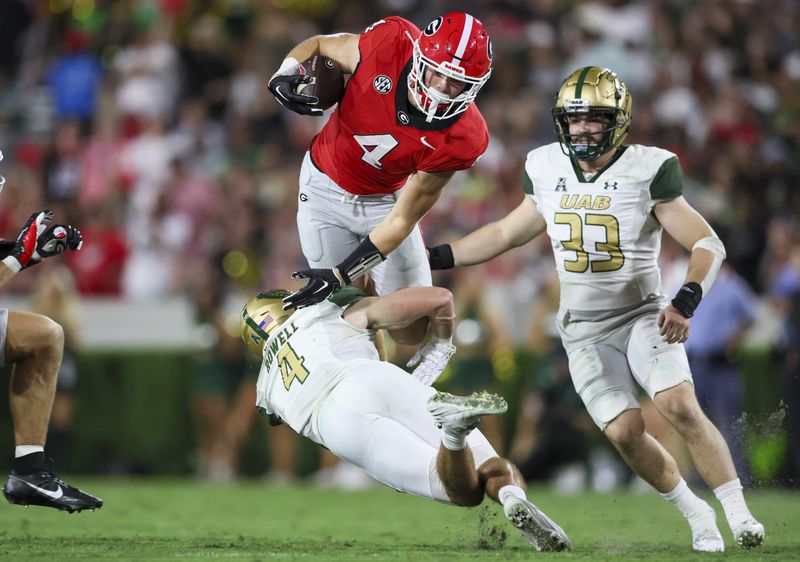 Georgia tight end Oscar Delp (4) leaps over the tackle attempt of UAB safety Ike Rowell (4) during the second quarter at Sanford Stadium, Saturday, September 23, 2023, in Athens, Ga. (Jason Getz / Jason.Getz@ajc.com)