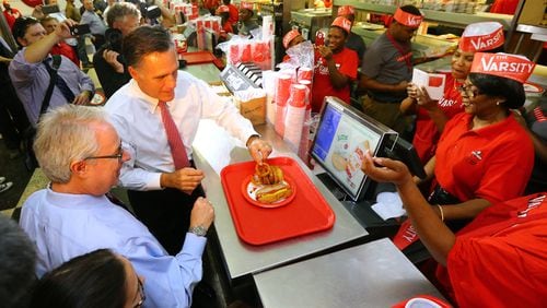 Former presidential hopeful Mitt Romney digs into the onion rings stumping in Georgia for Attorney General Sam Olens (left), joining Olens for lunch at The Varsity on Wednesday, Oct. 1, 2014, in Atlanta. CURTIS COMPTON / CCOMPTON@AJC.COM