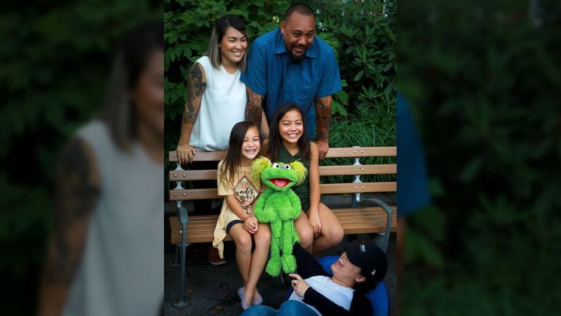 This Aug. 6, 2019 photo shows Jaana, standing left, and Sam Woodbury, from Irvine, California, and their daughters Salia, 10, seated right, and Kya, 6, with "Sesame Street" muppet Karli and puppeteer Haley Jenkins in New York.