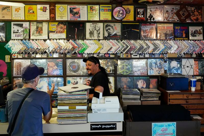 Tim Stamper, right, owner at Tracks In Wax record shop, talks with customer Michael Iffland, left, Thursday, April 18, 2024, in Phoenix. Special LP releases, live performances and at least one giant block party are scheduled around the U.S. Saturday as hundreds of shops celebrate Record Store Day amid a surge of interest in vinyl and the day after the release of Taylor Swift's latest album. (AP Photo/Ross D. Franklin)