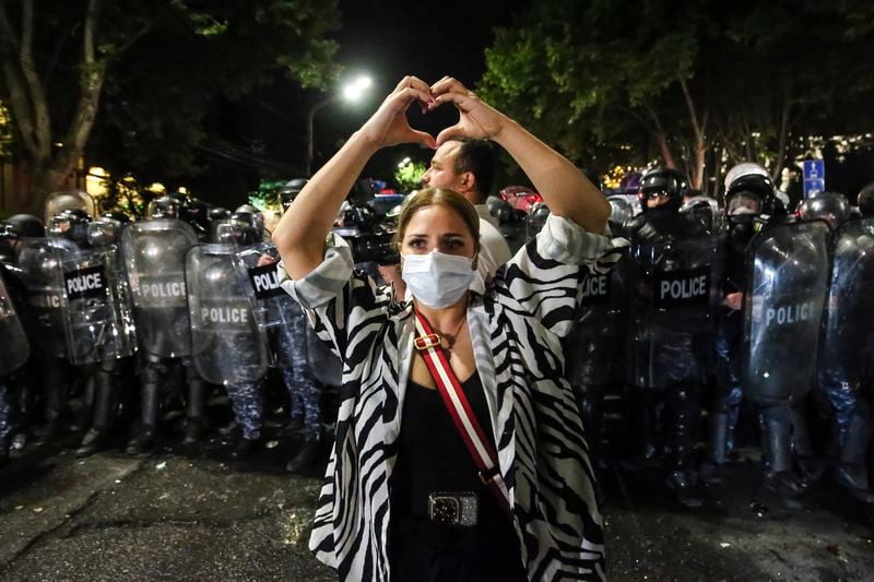 A woman shows a heart standing in front of riot police during an opposition protest against "the Russian law" near the Parliament building in Tbilisi, Georgia, on Wednesday, May 1, 2024. Clashes erupted between police and opposition demonstrators protesting a new bill intended to track foreign influence that the opposition denounced as Russia-inspired. (AP Photo/Zurab Tsertsvadze)