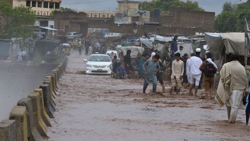 People wade through a flooded bridge on a stream, which is overflowing following heavy rains, on the outskirts of Peshawar, Pakistan, Monday, April 15, 2024. Lightnings and heavy rains killed dozens of people, mostly farmers, across Pakistan in the past three days, officials said Monday, as authorities declared a state of emergency in the country's southwest following an overnight rainfall to avoid any further casualties and damages. (AP Photo/Muhammad Sajjad)