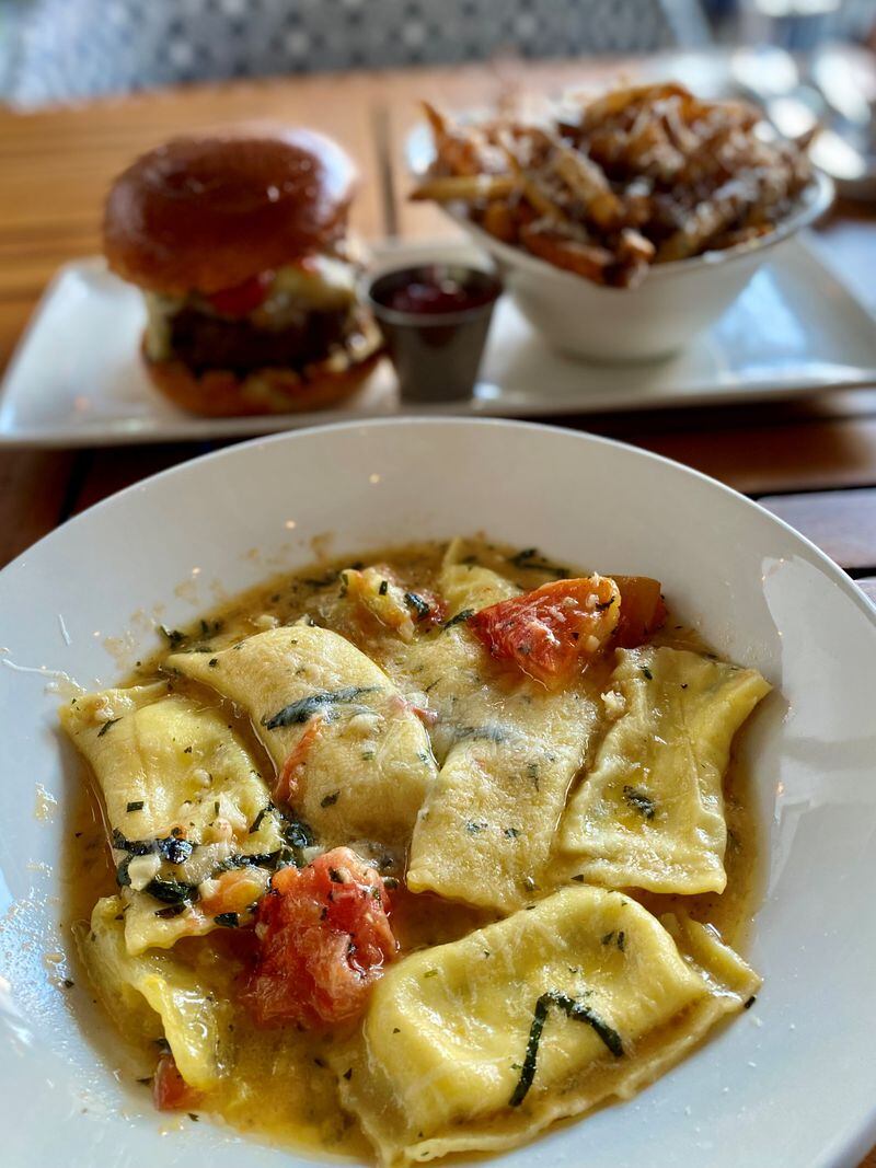 Fresh summer basil and tomato brighten the lemon and herb ricotta-filled ravioli at Seed Kitchen & Bar. The famous Merchant Burger with Parmesan fries is in the background. (Wendell Brock for The Atlanta Journal-Constitution)