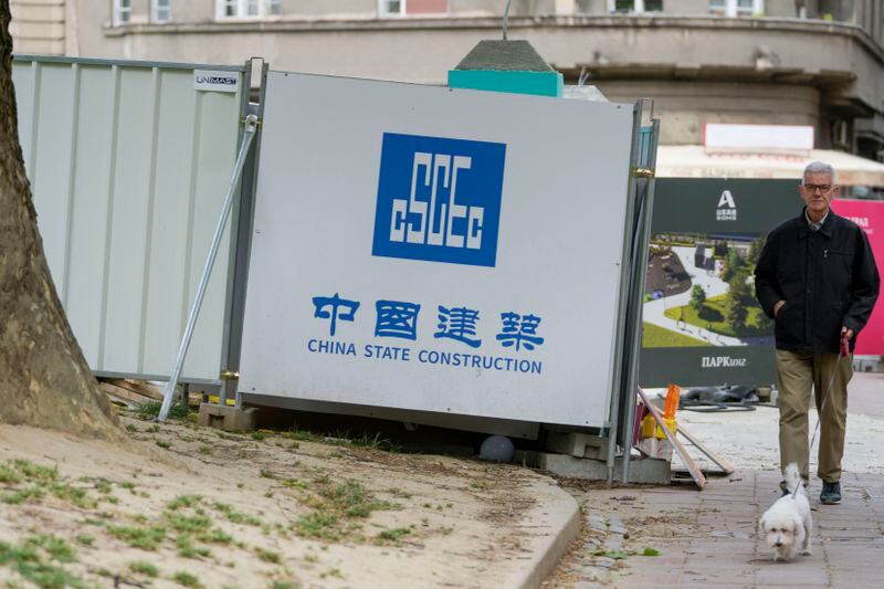 A man with a dog walks by a construction site in Belgrade, Serbia, Wednesday, May 1, 2024. Chinese President Xi Jinping will visit France, Serbia and Hungary this week as Beijing appears to seek a larger role in the conflict between Russia and Ukraine that has upended global political and economic security. (AP Photo/Darko Vojinovic)